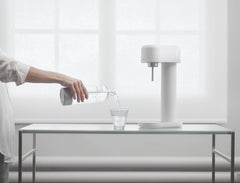 A white and silver ruby 2 in front of a window and a hand pouring a glass of water#väri_white-silver