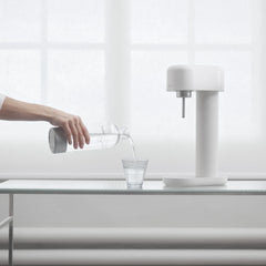 A white and silver ruby 2 in front of a window and a hand pouring a glass of water