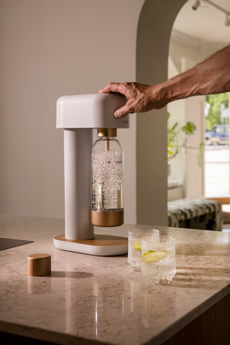 A male arm reaching out from the right to carbonate fresh water using a white-copper Ruby 2 sparkling water maker