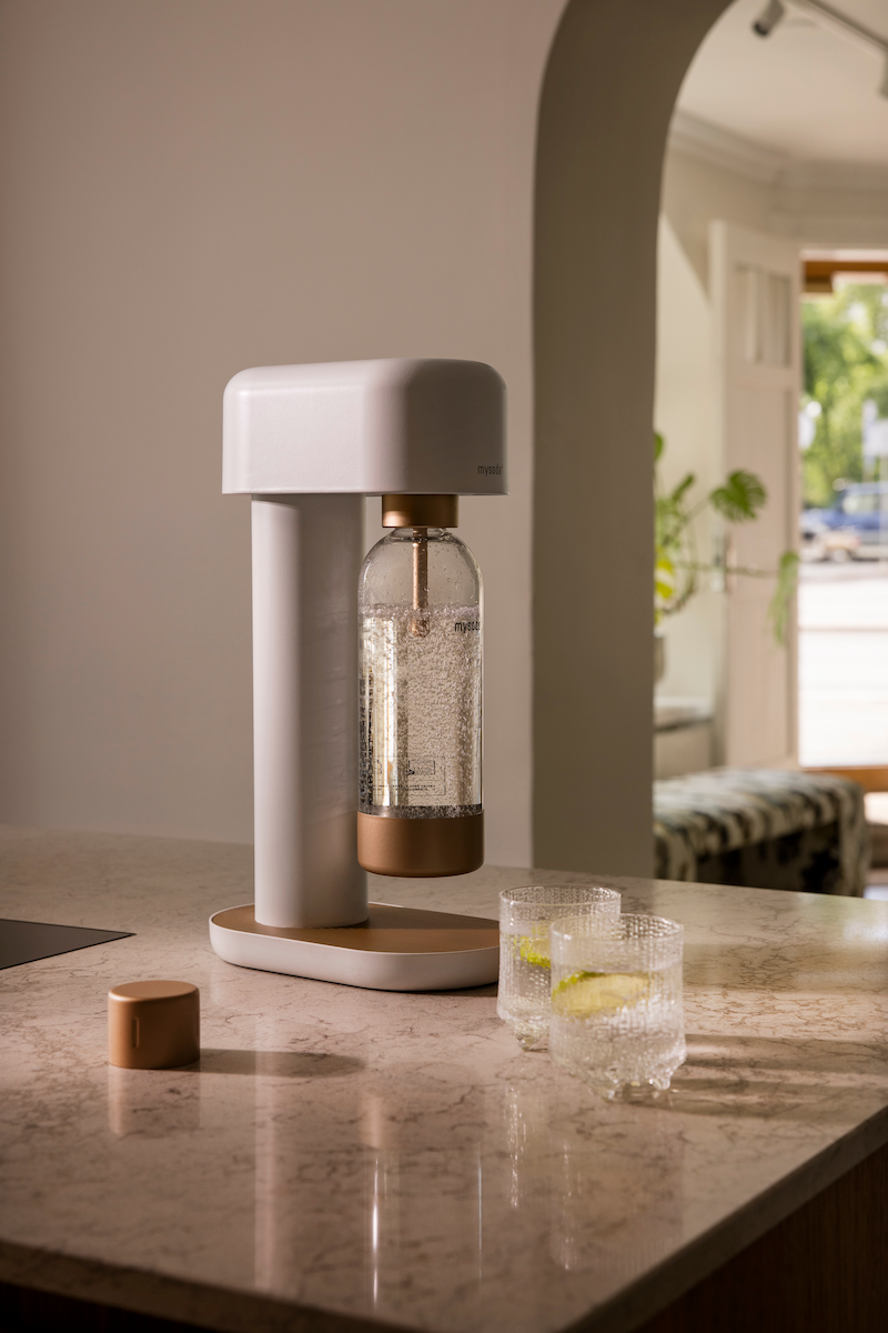 A white-copper Ruby 2 soda maker and two glasses of sparkling water on a marble countertop