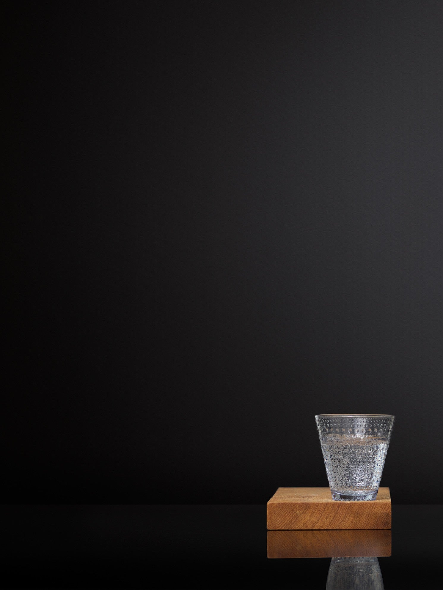 A glass of water on a small wooden tray in front of black background