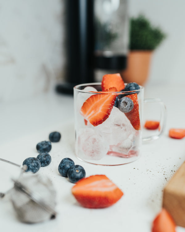 A glass filled with ice cubes, blueberries, and raspberries