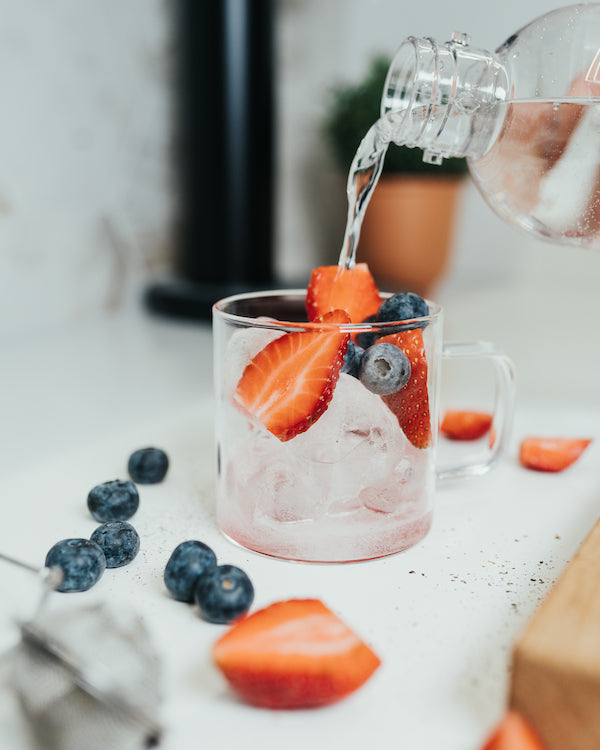 Sparkling water is added to a glass of berries and ice cubes