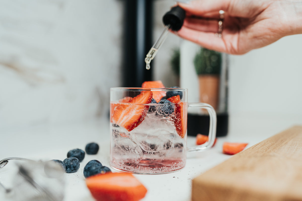 Liquid sweetener being added to a blass of berry iced tea with sparkling water and fresh berries