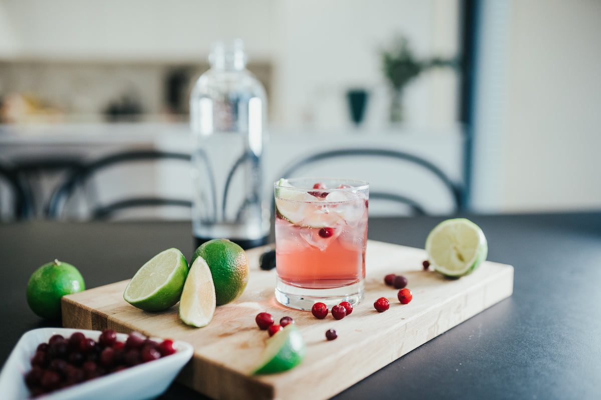 A glass of cranberry mocktail on a board with lime fresh wedges and cranberries