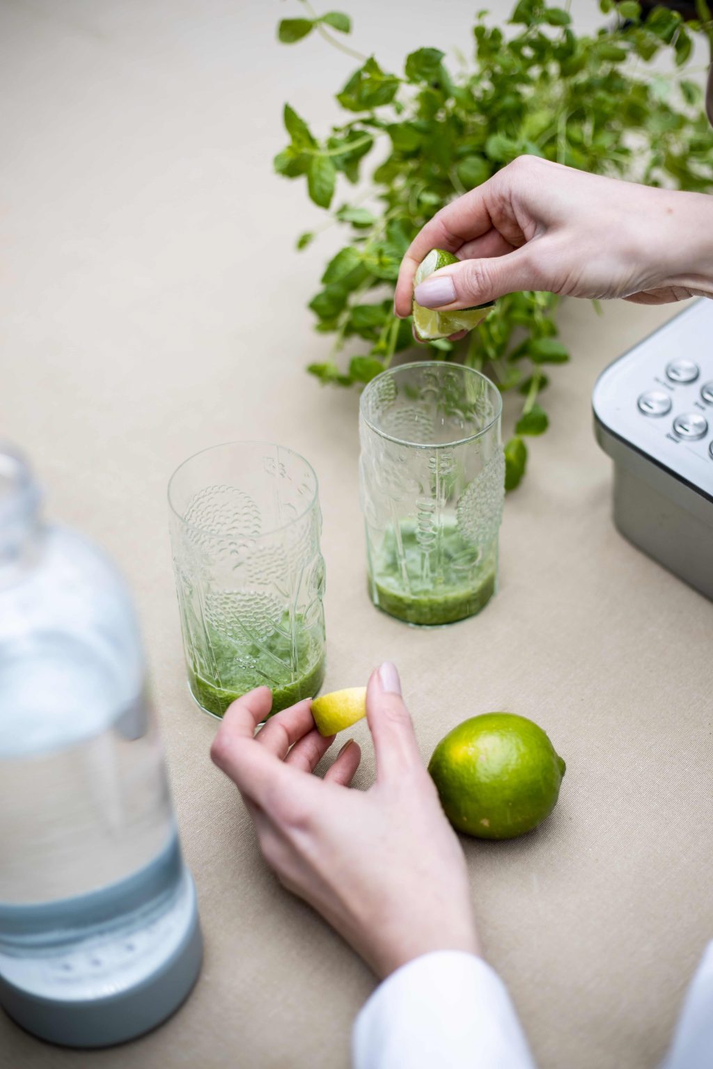 Lime being squeezed into glasses while preparing cucumber lime mocktails