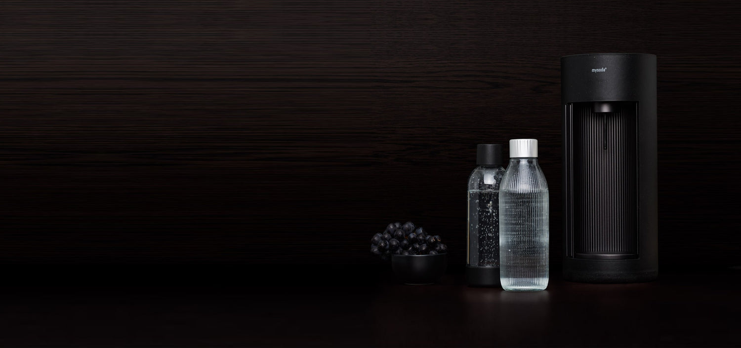 A glassy sparkling water maker, colour black, a PET bottle and a glass bottle in front of black background