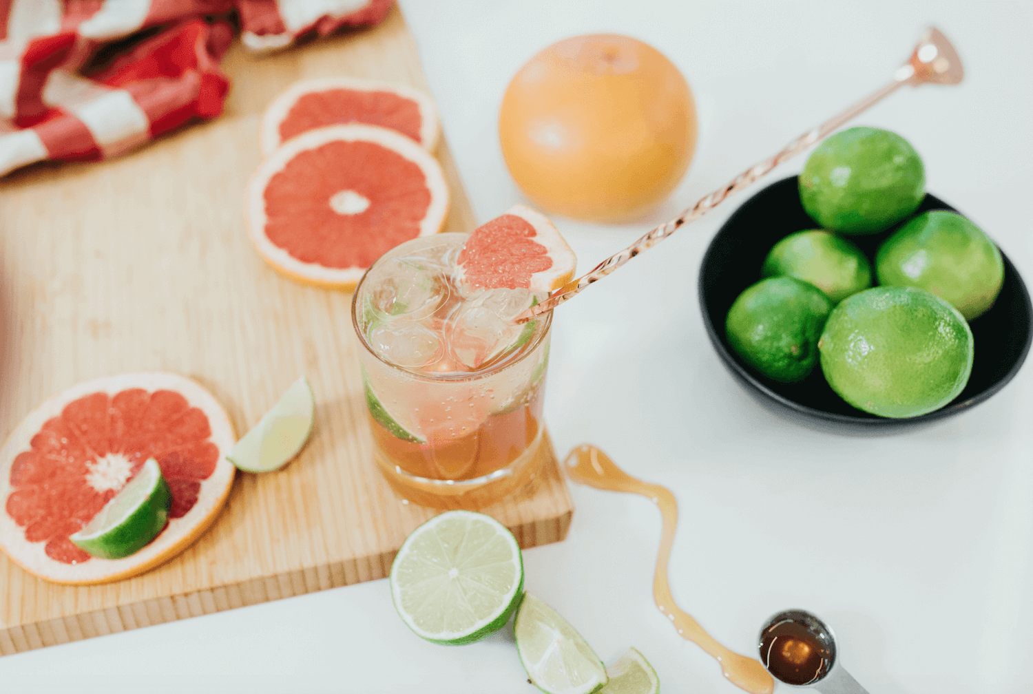 A glass of grapefruit lime mocktail on a wooden board surrounded by grapefruit slices and pieces of lime