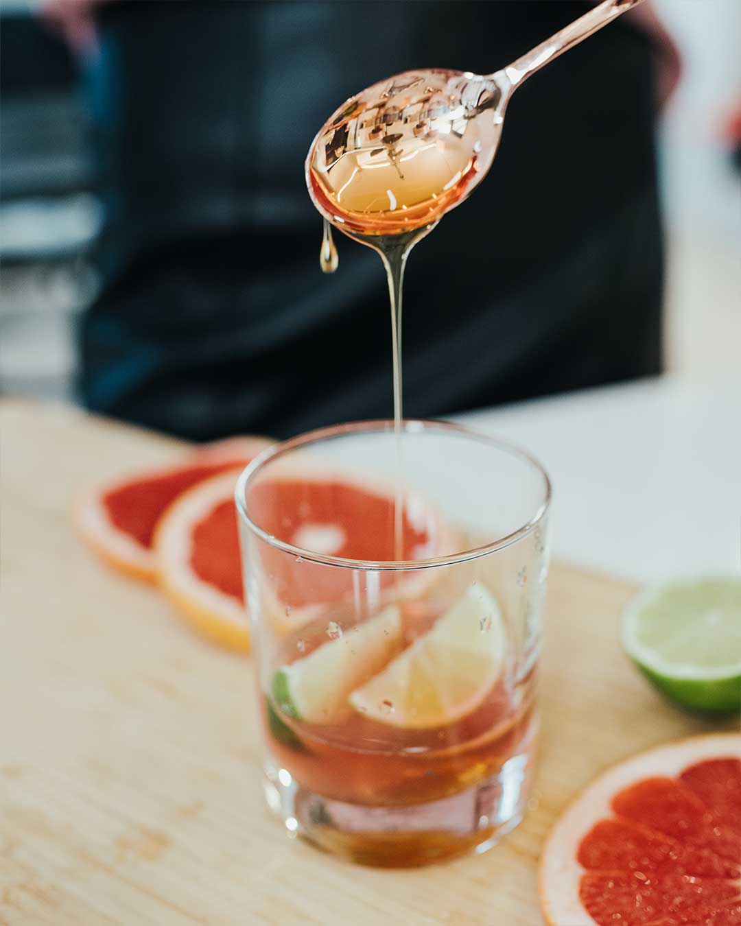 Sweetener being added to a glass with lime wedges for preparing a fruity fizzy drink