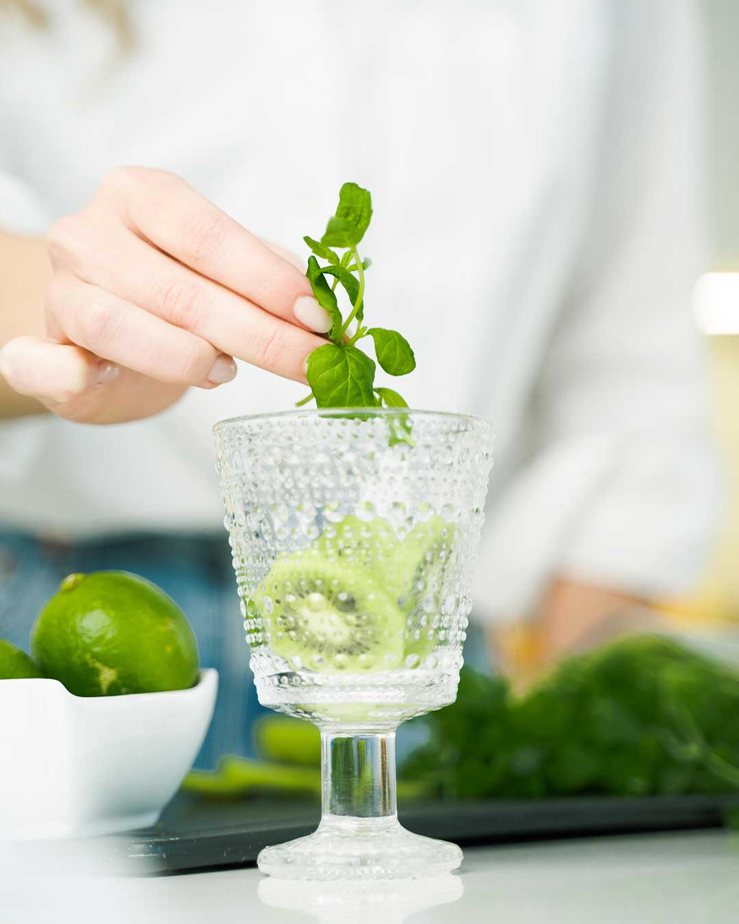 Kiwi slices and greens being added to a glass