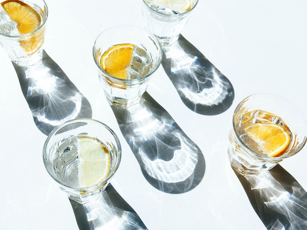 Glasses of sparkling water decorated with slices of orange and lime. The glasses break the bright sunlight