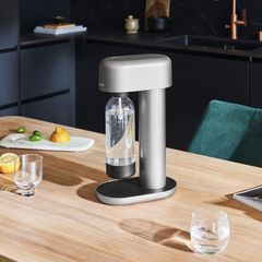 A silver Ruby soda machine on a wooden kitchen table in a black kitchen