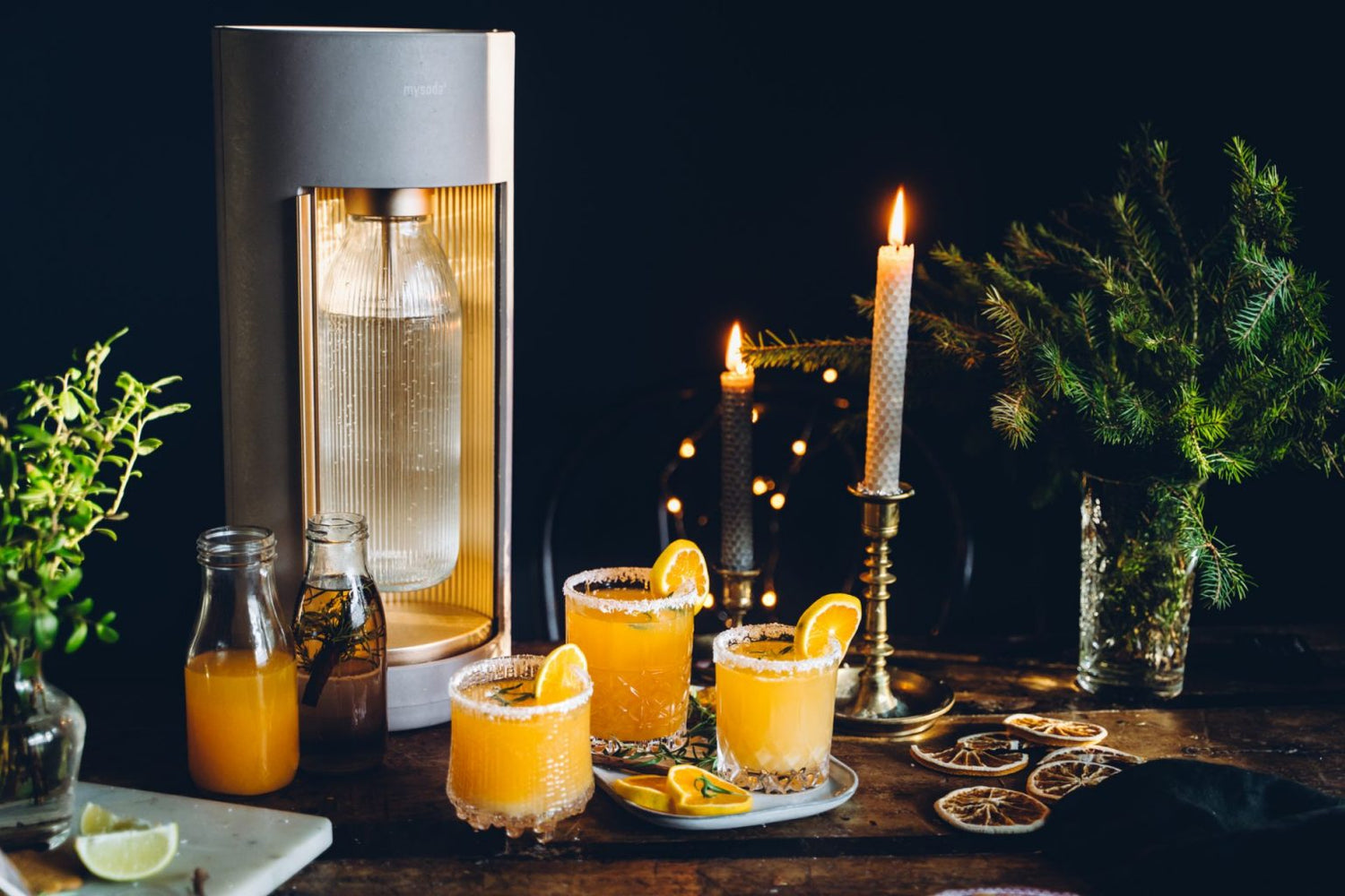 Three glasses of festive tangerine mocktail next to a latte-coloured Mysoda Glassy sparkling water maker in a festive Christmas setting