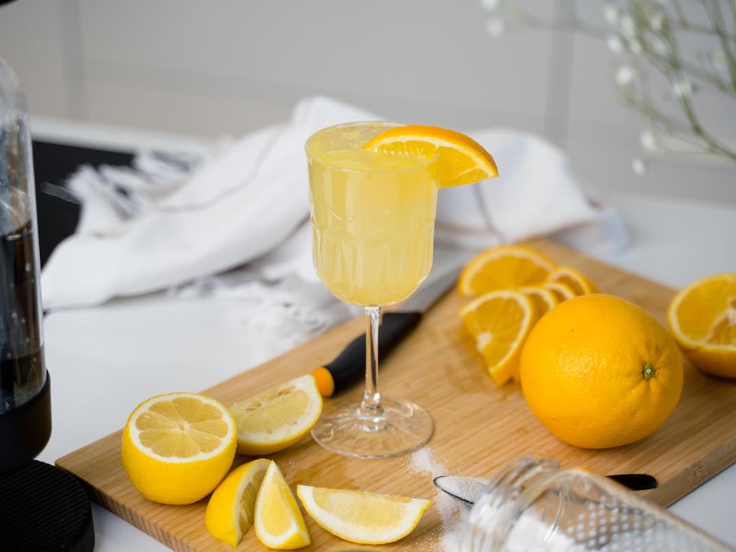 A glass of orange-lemon-mocktail on a board with slices of orange and lemon spread around it