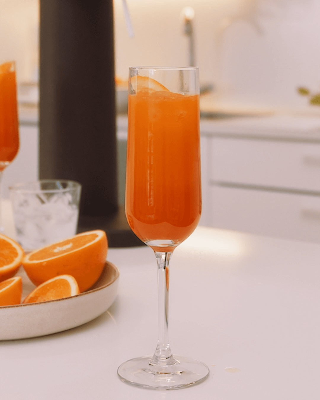 A tall glass of fresh orange mocktail on a kitchen counter