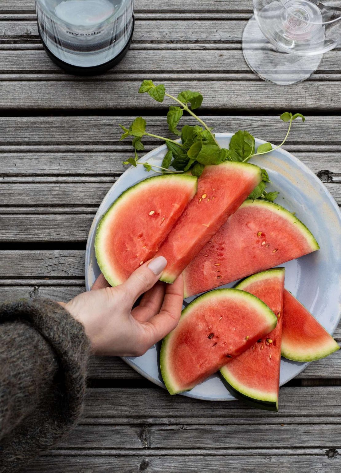 A hand reaching out to pick up one of several pieces of watermelon on a plate