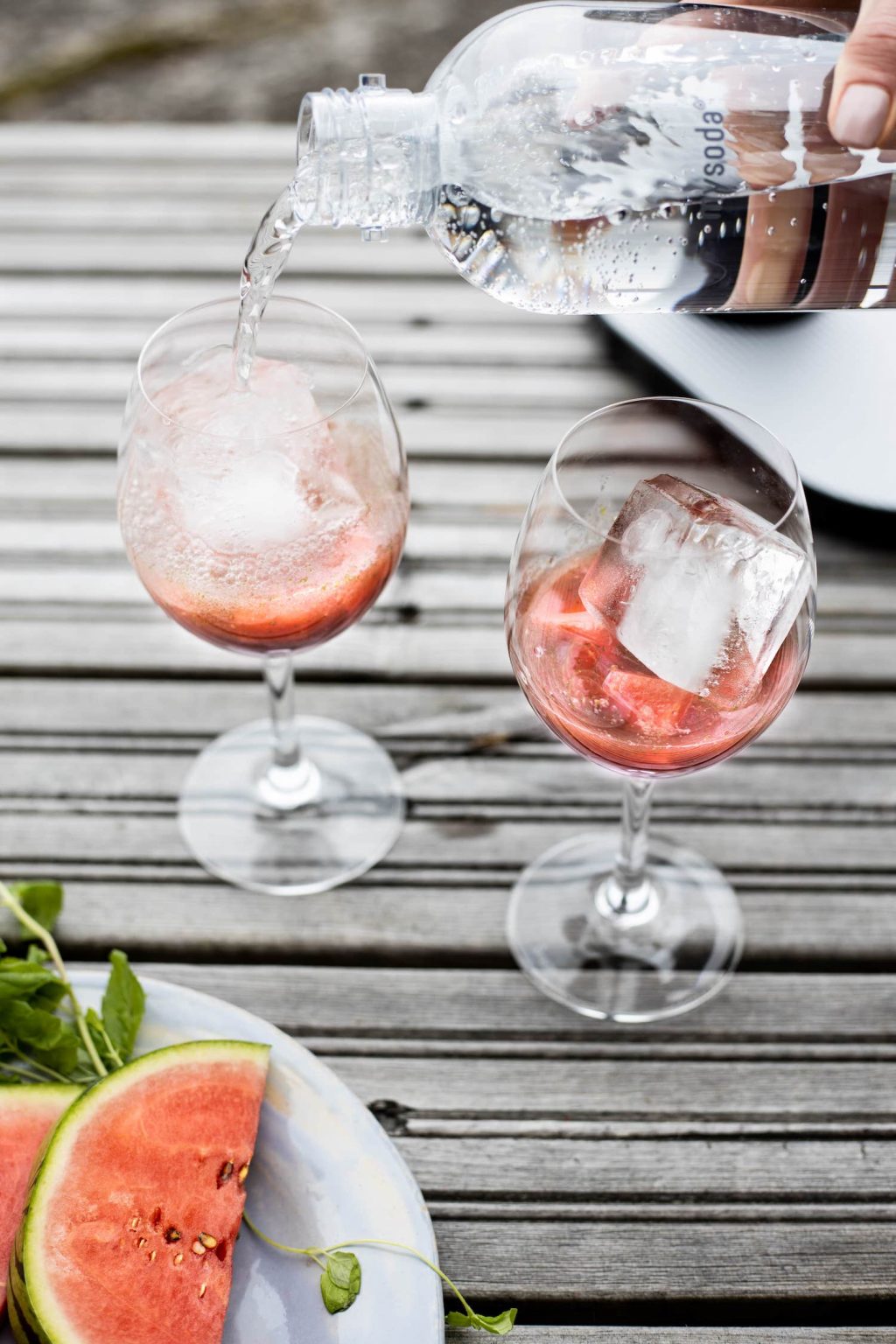 Water being poured into two glasses to finalize watermelon mocktails