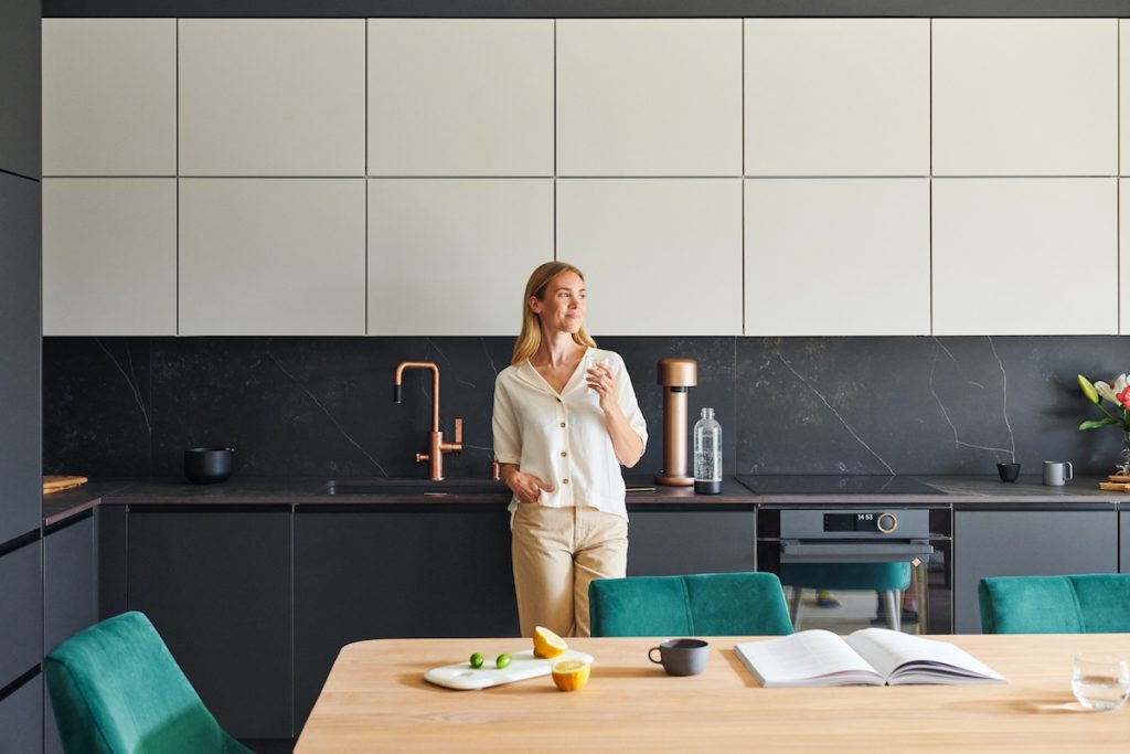 Woman standing in a black kitchen drinking sparkling water