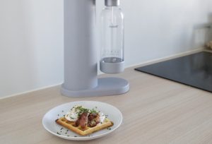 A plate of delicious savoury breakfast waffles in front of a Mysoda Woody sparkling water maker on the kitchen counter.